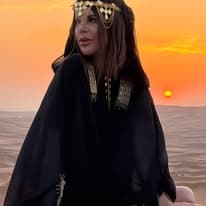 Guest in a black and gold abaya standing before a blazing orange desert sunset